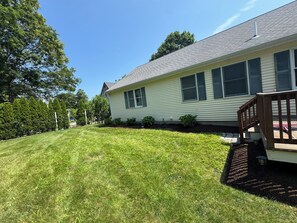 A residential house with a well-maintained lawn, a wooden deck, and a clear sky. - High Tide Hideaway - 3-bedroom house in Sagamore Beach walking distance to beach (Bourne)