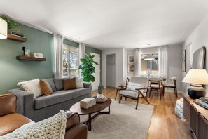 Un salon avec un canapé gris, une table basse et un coin repas comprenant une table et des chaises.