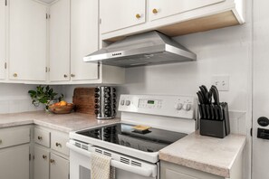A modern kitchen with white cabinets, a stainless steel range hood, a built-in oven, and a countertop with a knife block. - Dog-Friendly Arvada Home with Fire Pit, 18 Min to Red Rocks & Near Denver (Arvada)