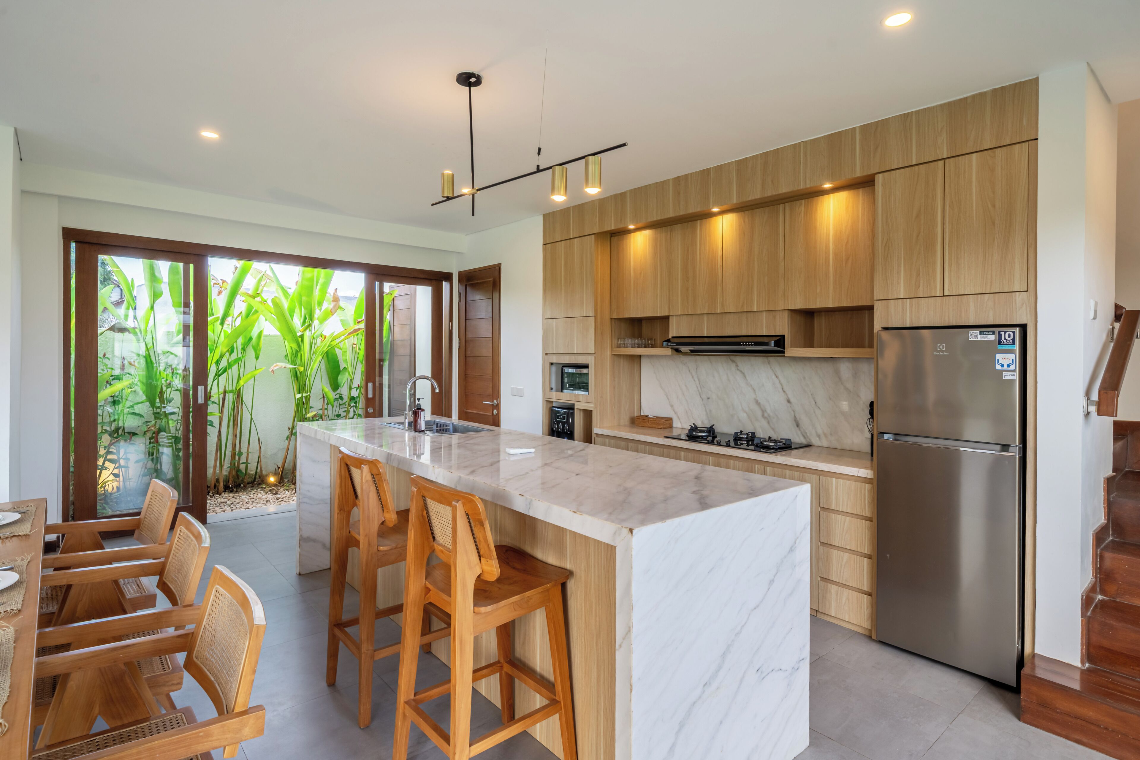 Una cocina moderna con una isla de mármol, taburetes de madera y un refrigerador de acero inoxidable.