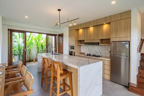Uma cozinha moderna com uma ilha de mármore, banquetas de madeira e uma geladeira de aço inoxidável.