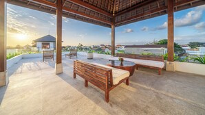 Un espace extérieur aménagé, abrité et doté de bancs et d’une table, offrant une vue sur un quartier résidentiel avec ses maisons et un plan d’eau.