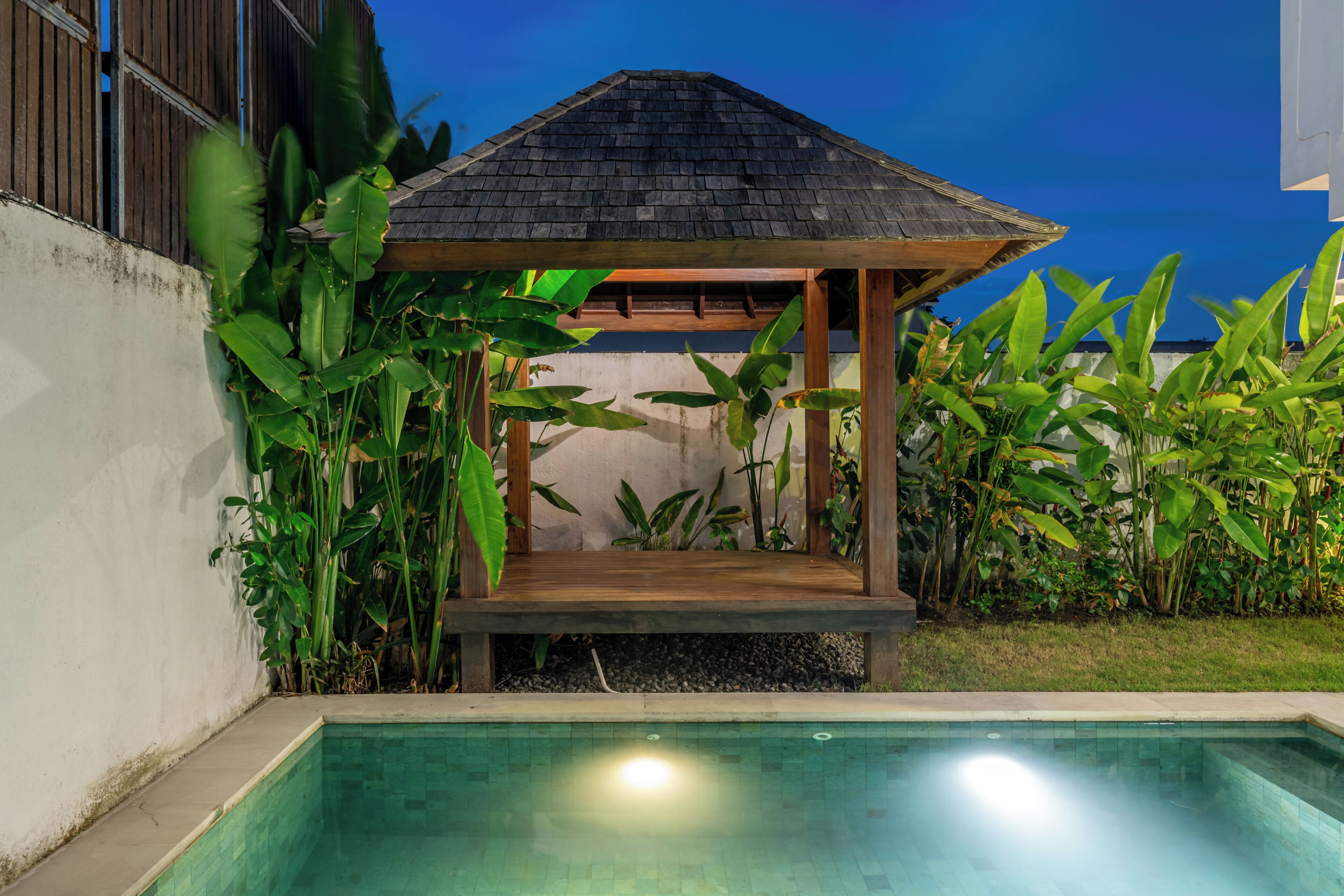 A poolside area with a wooden gazebo and lush tropical plants.