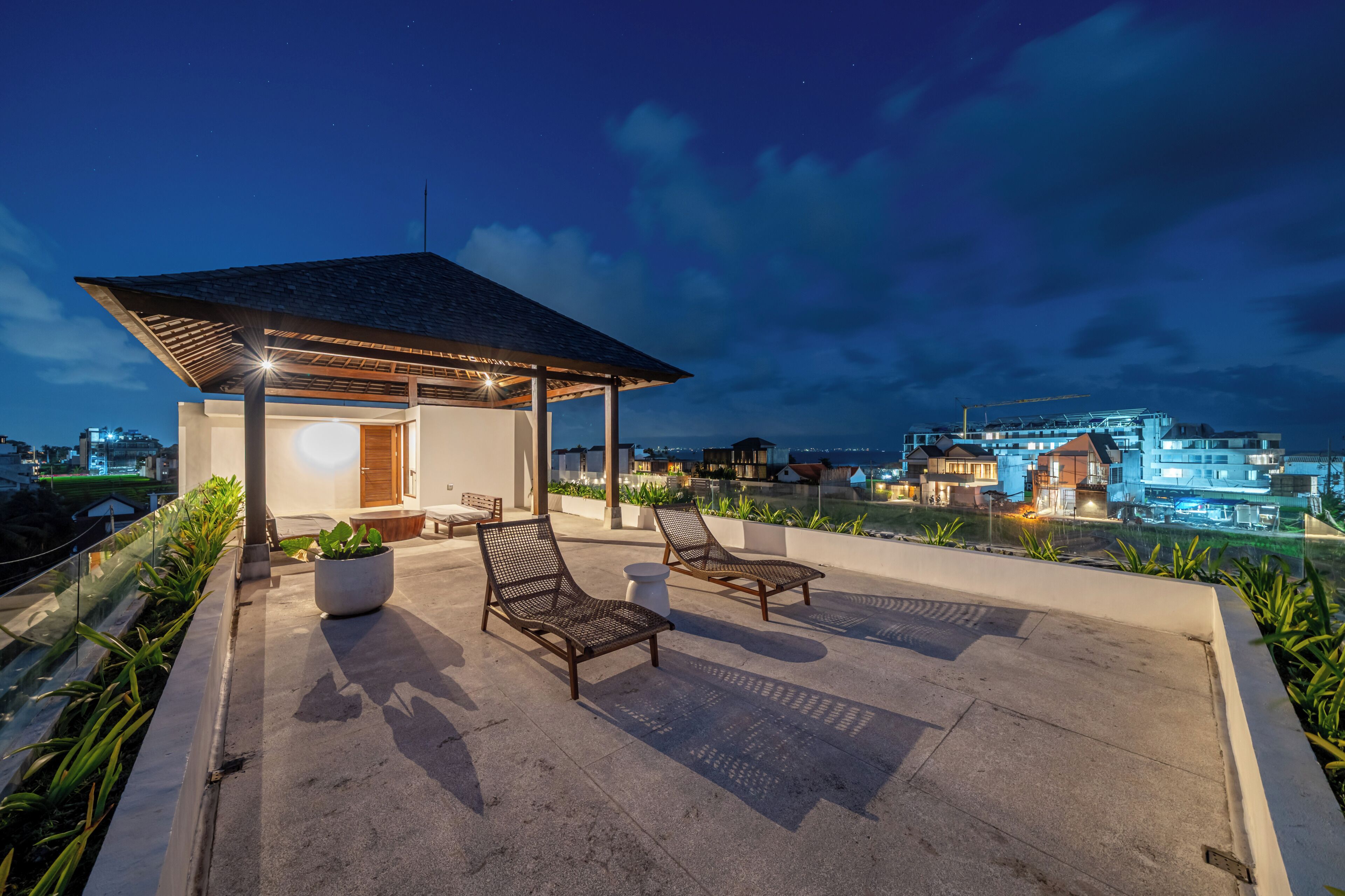 Una terraza en la azotea con dos sillones de lounge, un espacio cubierto para sentarse y vistas del paisaje urbano al atardecer.