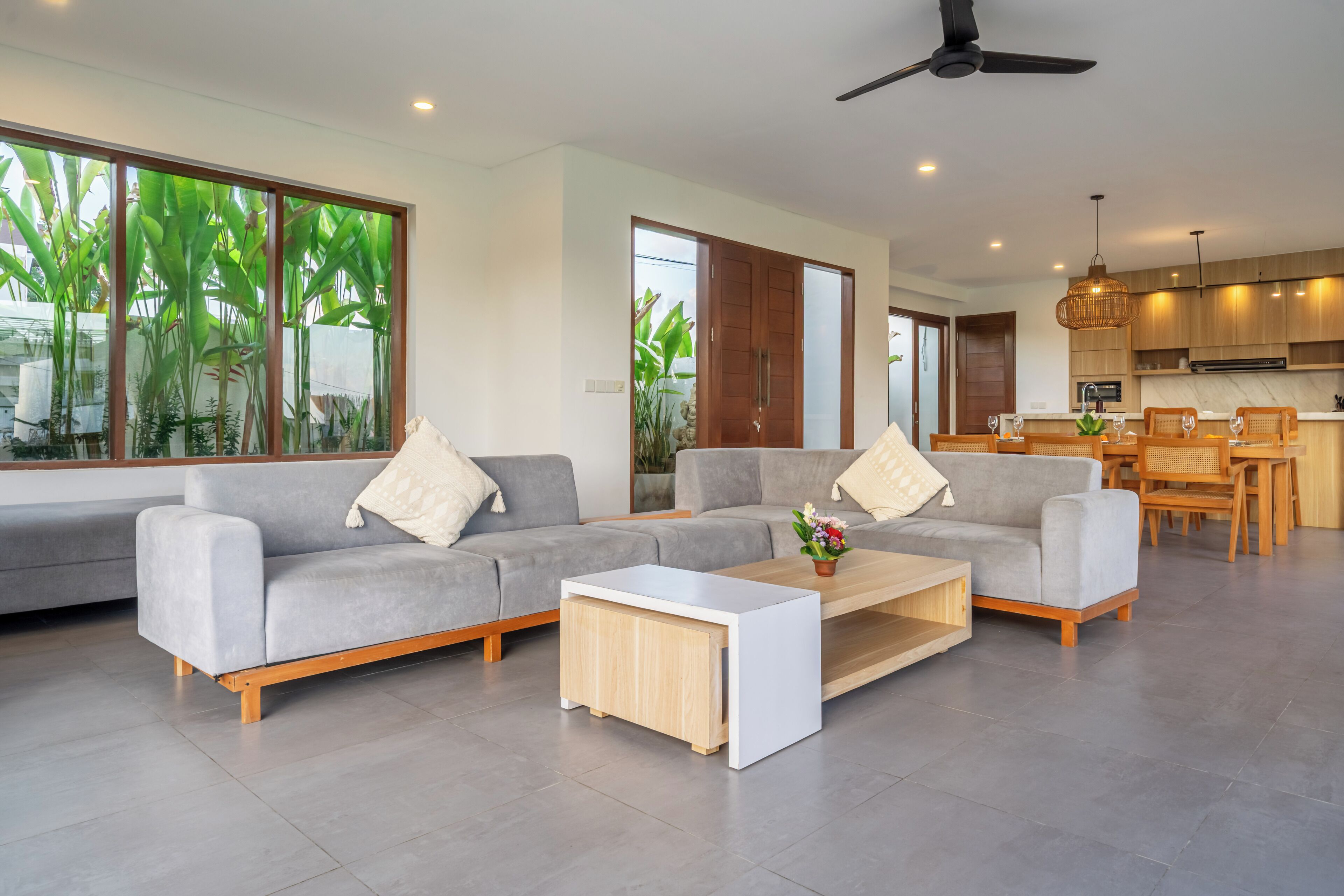 A modern living room with a grey sectional sofa, a coffee table, and a dining area with wooden chairs and a table.