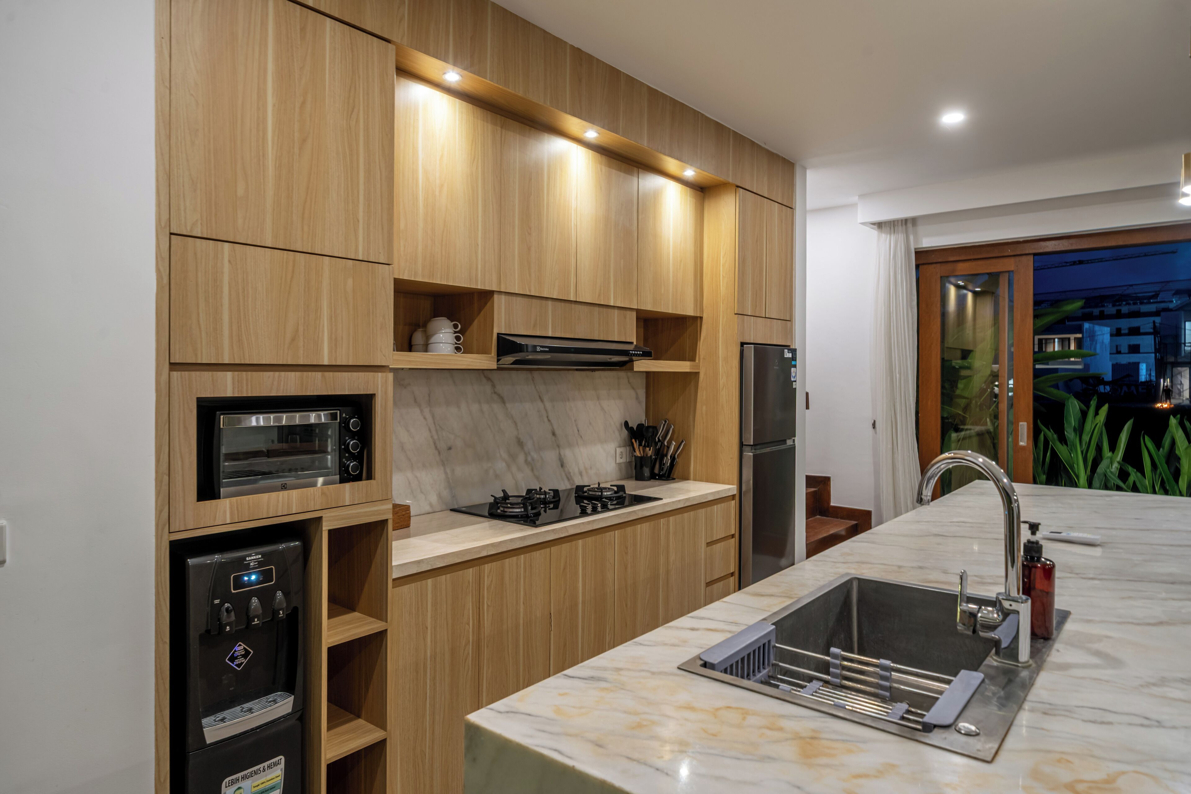 Una cocina moderna con electrodomésticos integrados, encimera de mármol y muebles de madera.