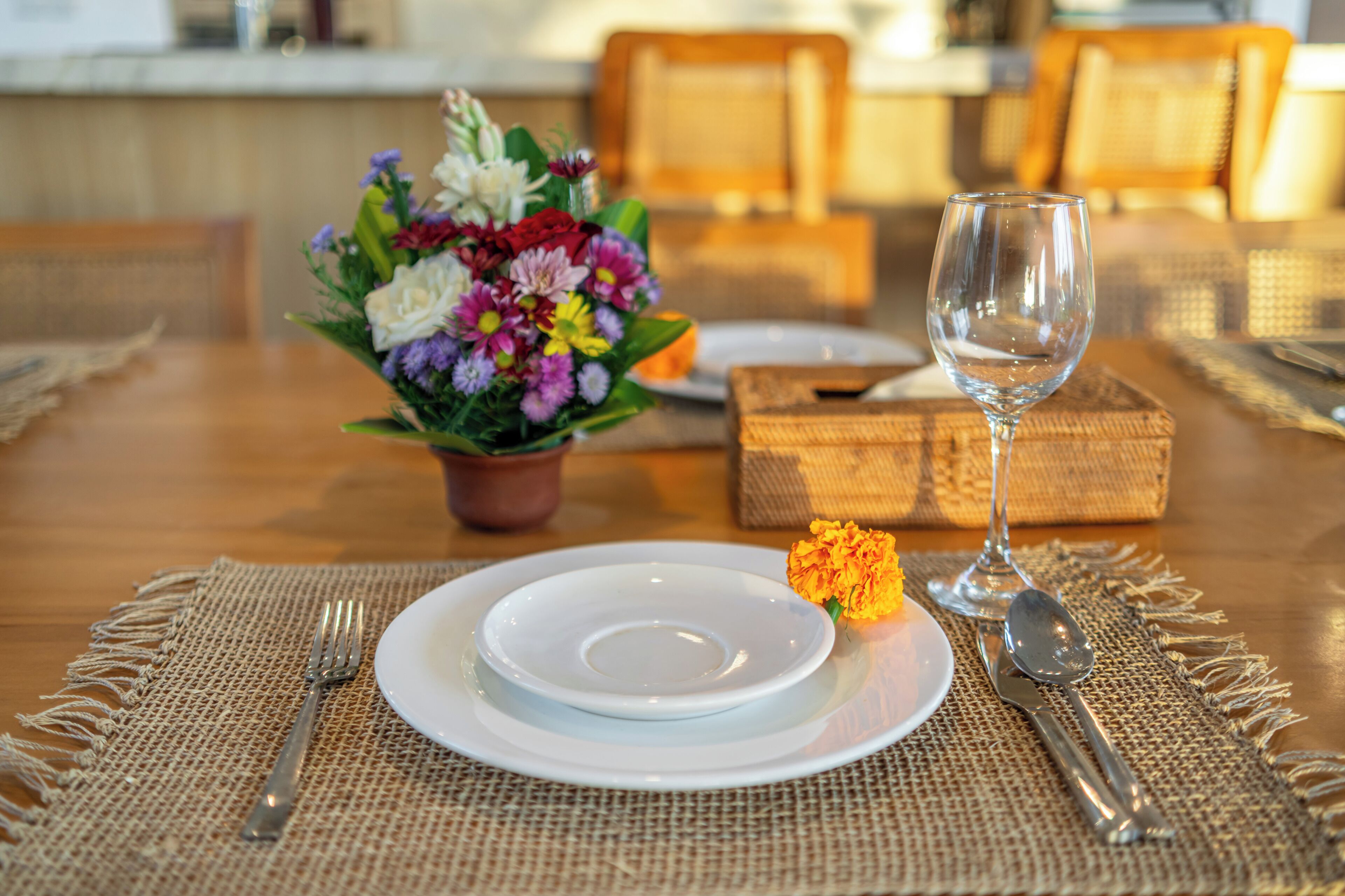 Una mesa de comedor dispuesta con platos, cubiertos, una copa, un pequeño jarrón con flores y una caja.