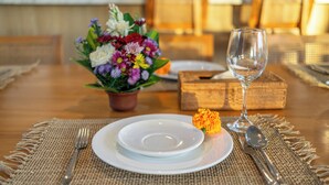 Une table à manger dressée avec des assiettes, des couverts, un verre, un petit vase avec des fleurs et une boîte.