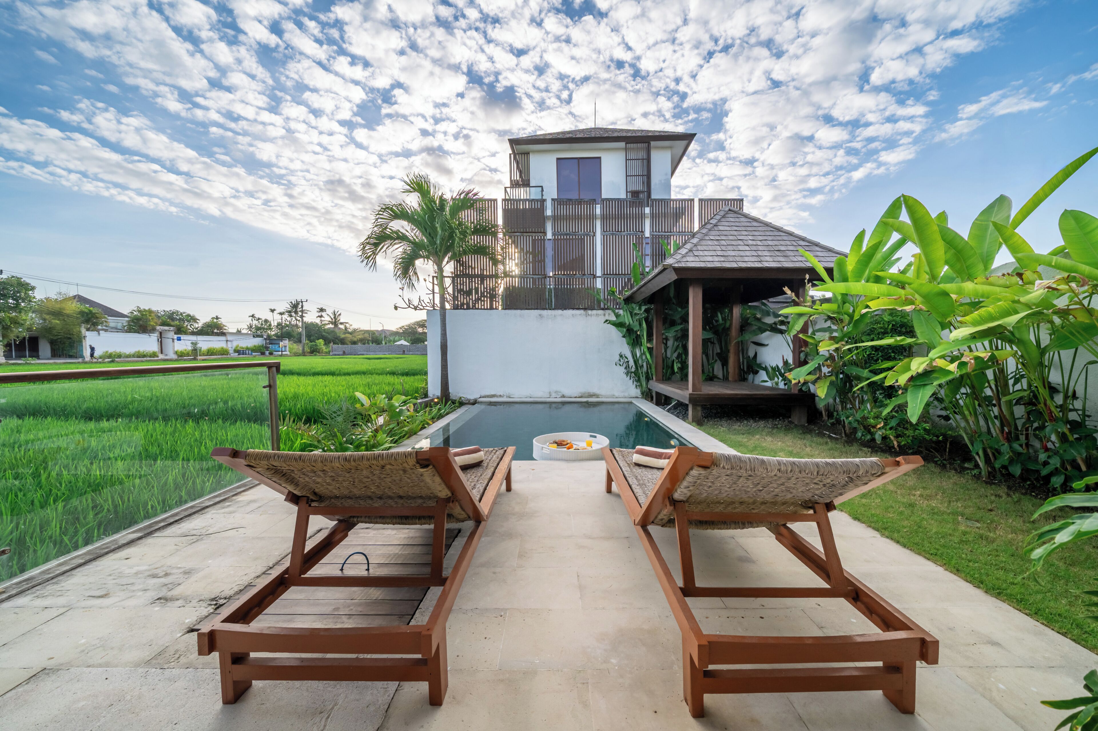 A poolside area with two lounge chairs facing a pool, surrounded by greenery and a view of a residential building.