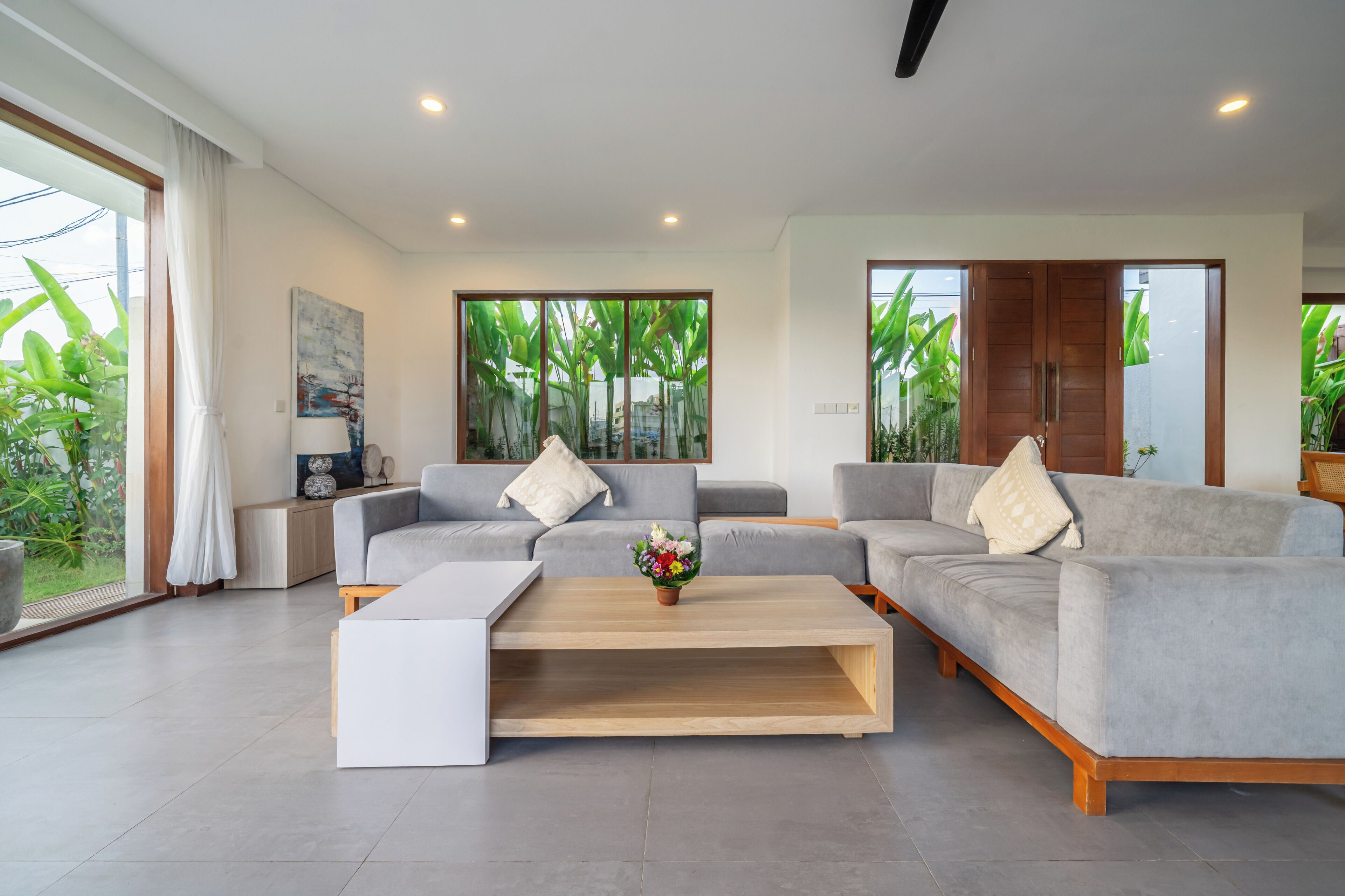 A modern living room with grey sofas, a coffee table, and a large window with a view of greenery.