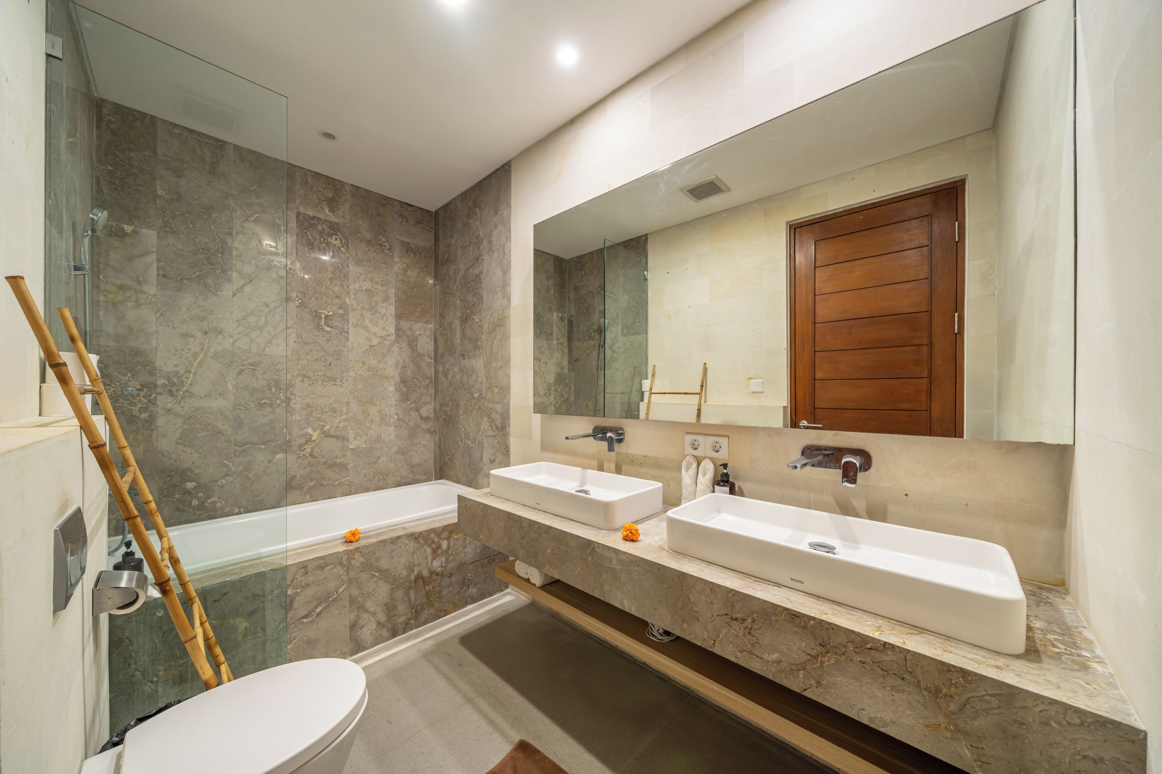A modern bathroom with two sinks, a glass shower enclosure, and a wooden door.