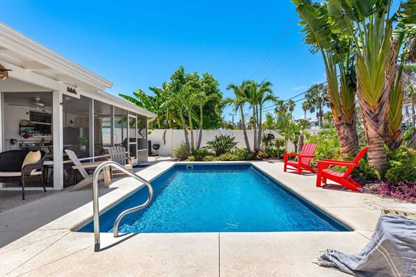 Ein Schwimmbecken mit überdachter Terrasse, roten Stühlen und tropischen Pflanzen.