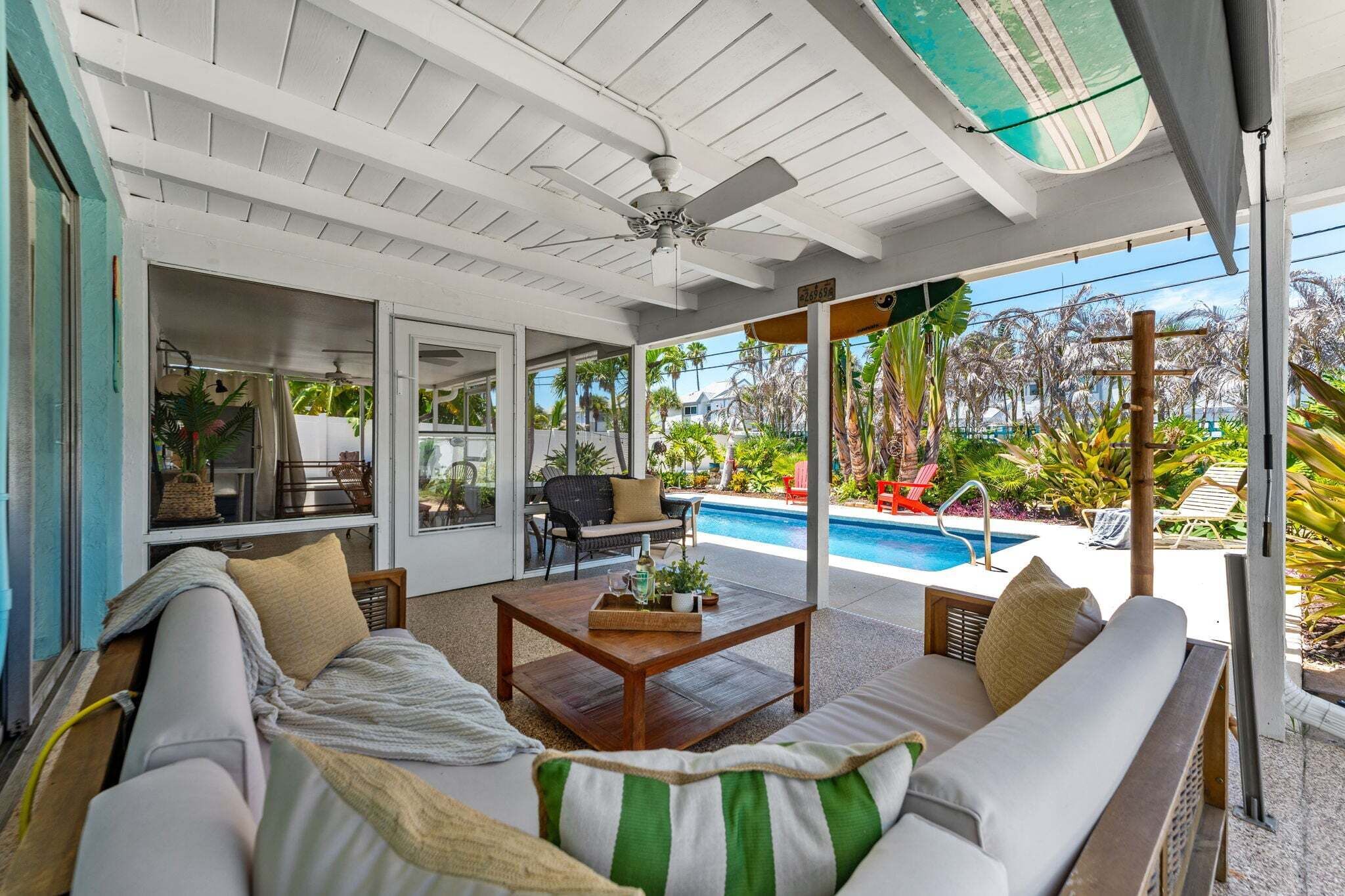 A covered outdoor seating area with a pool, furnished with sofas and a coffee table.