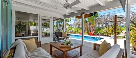 A covered outdoor seating area with a pool, furnished with sofas and a coffee table.