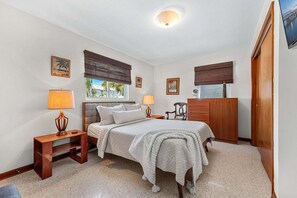 Ein Schlafzimmer mit einem Bett, Nachttischen, einem Schminktisch und einem Fenster mit Jalousien.