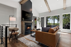 A modern living room with a fireplace, a sofa, a coffee table, and a view of the outdoors. - Modern Luxury-Couples Retreat-Hot Tub-Private Gym-Speakeasy-Close to Downtown (Blue Ridge)