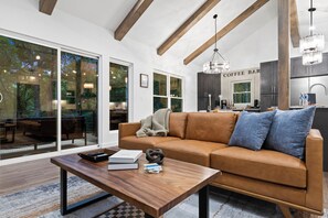 A modern living room with a brown leather sofa, a wooden coffee table, and a large window with a view of trees. - Modern Luxury-Couples Retreat-Hot Tub-Private Gym-Speakeasy-Close to Downtown (Blue Ridge)