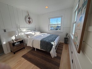 A bedroom with a bed, bedside table, lamp, and a window with a view of the outside.