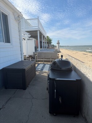 A patio area with a grill, a wooden bench, and a view of the beach. - Lake Huron Cottage - Walkout Beachfront - Sleeps 8 (Kawkawlin)