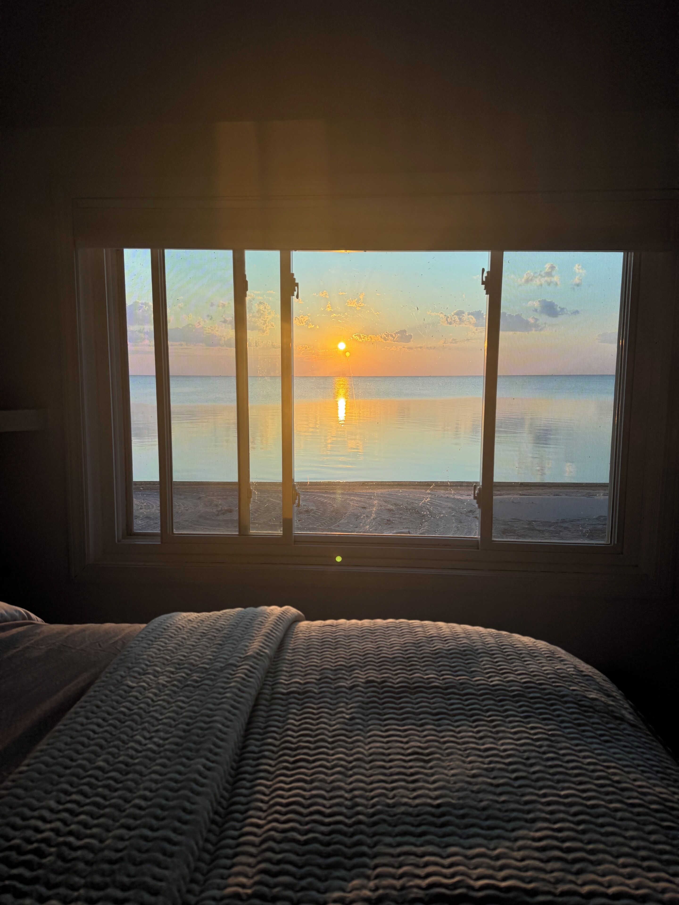 Una habitación con un amplio ventanal con vistas a una playa al atardecer.