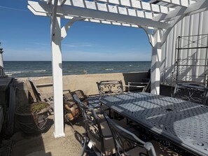 A covered outdoor seating area with a view of the ocean, metal chairs, a table, and a pergola structure.