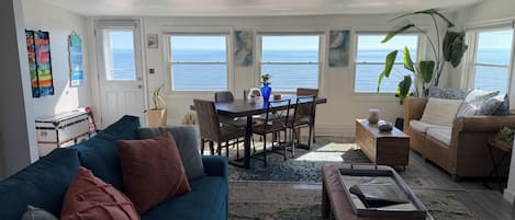 A spacious living area with a view of the ocean, a dining table with chairs, a sofa, and a coffee table.