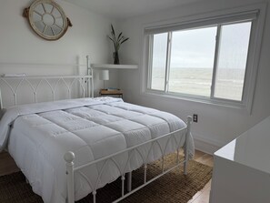 A bedroom with a bed, a window, a plant, and a wall-mounted decoration. - Lake Huron Cottage - Walkout Beachfront - Sleeps 8 (Kawkawlin)