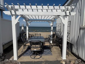 Un porche cubierto con una mesa y sillas, con vista a la playa.