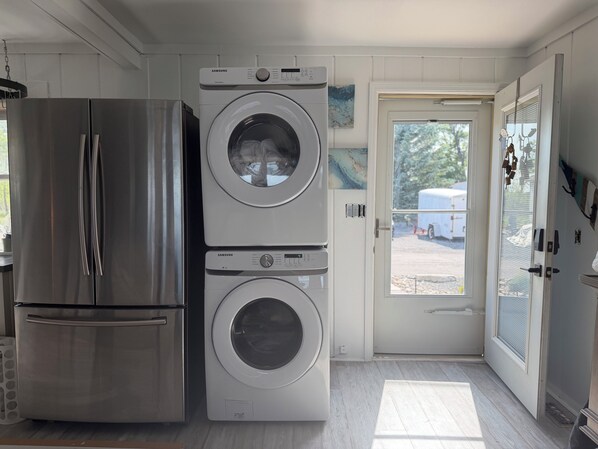 A compact kitchen with a stainless steel refrigerator, a Samsung washing machine, and a door leading to an outdoor area.