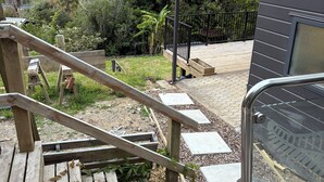 Eine Holzterrasse mit Metallgeländer, die zu einem Balkon mit Blick auf einen üppigen, grünen Hügel führt.