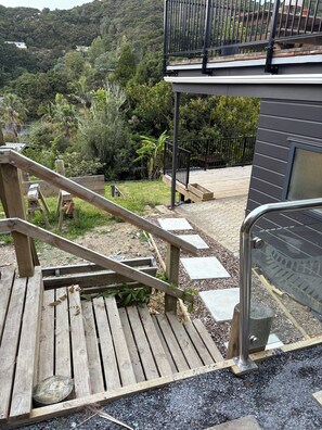Una terraza de madera con baranda de metal, que conduce a un balcón con vistas a una ladera verde y exuberante.