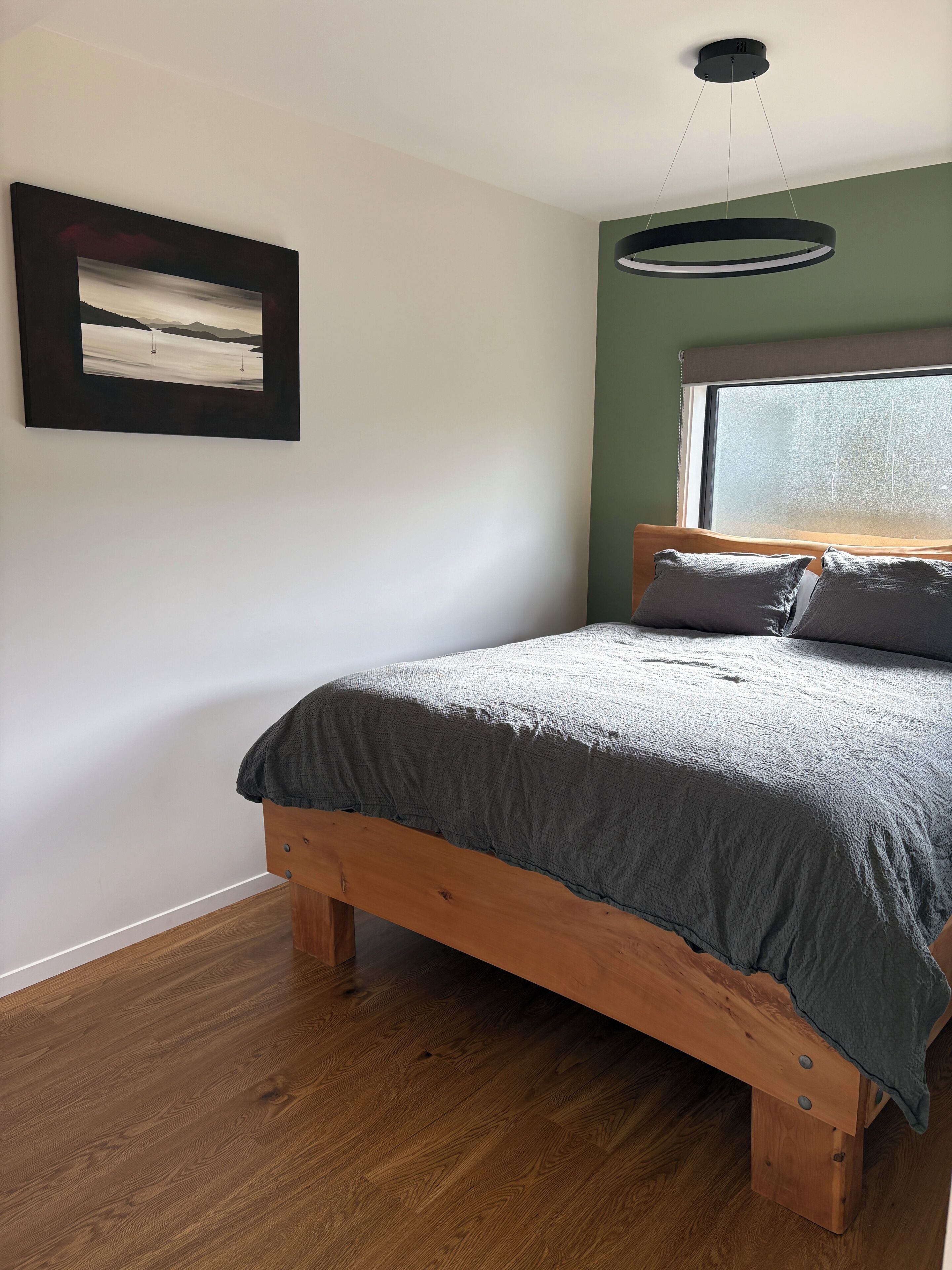 A bedroom with a wooden bed, a framed picture on the wall, and a window with a view.