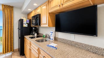 A kitchen with wooden cabinets, a black refrigerator, a microwave, a coffee maker, and a flat-screen TV.