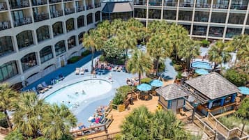 Een hotel met een centraal gelegen zwembad, omringd door palmbomen en een loungegebied.