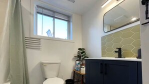 Une salle de bain comprenant des toilettes, une fenêtre avec des stores, un lavabo avec un miroir et un meuble de rangement.