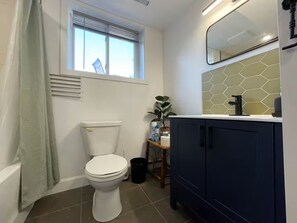 A bathroom with a toilet, a window with blinds, a sink with a mirror, and a cabinet.