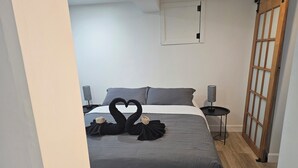 A hotel room with a bed, two bedside lamps, a wooden door, and a wall-mounted light fixture.