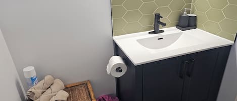 A bathroom with a white sink, a mirror, a towel rack, and a waste bin.