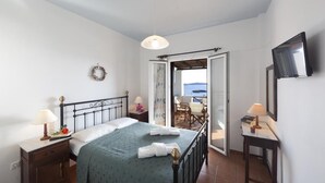 Ein Schlafzimmer mit einem Bett, Nachttischen, einem Fernseher und einer offenen Tür, die auf einen Balkon führt.