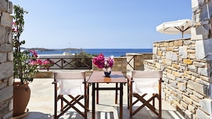 Ein Sitzbereich im Freien mit Tisch und Stühlen, einem Blumentopf und Blick auf das Meer.