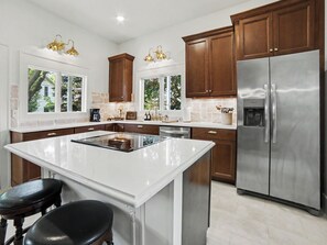A modern kitchen with a central island, stainless steel appliances, and wooden cabinets. - Coastal Grand 7 bed, 4 bath + hot tub & fire pit (Ludington)