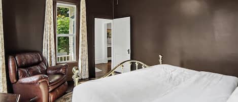 A bedroom with a bed, a leather armchair, a wooden nightstand, a ceiling fan, and a window with curtains.