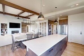A modern kitchen with a large island, wooden beams, pendant lighting, and a wine rack. - Sunlight home with private hot tub, game room and EV charger (Steamboat Springs)