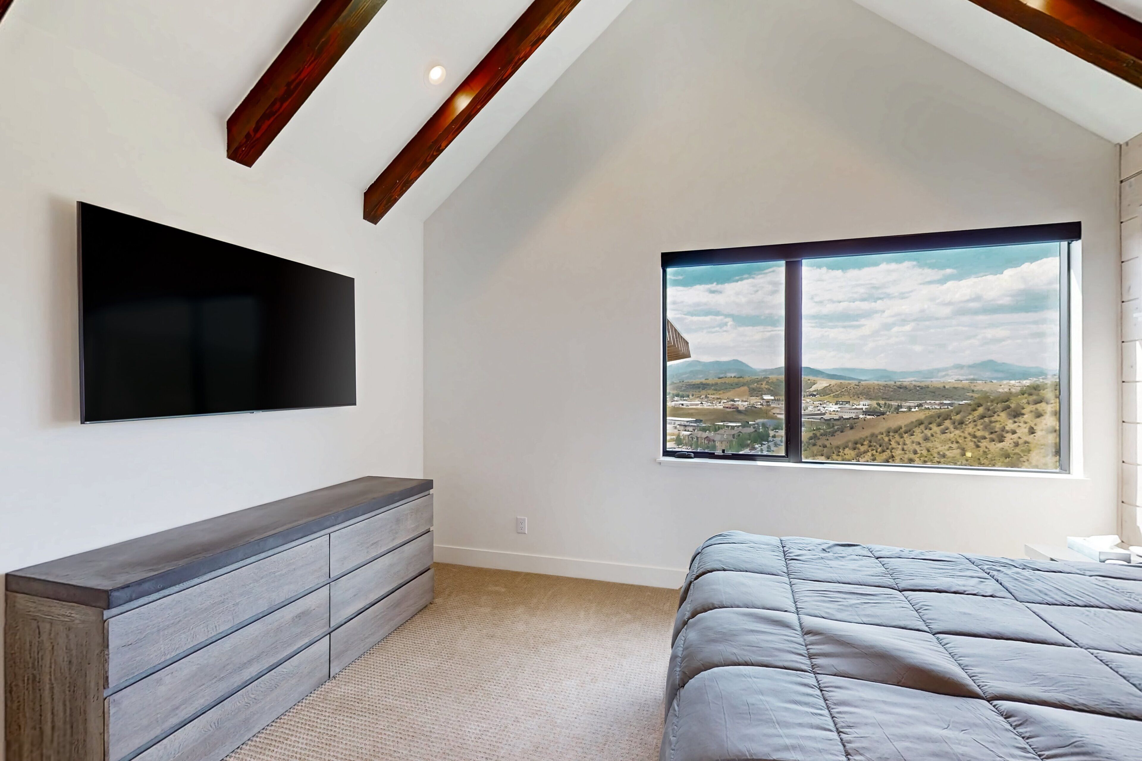 Une chambre avec une grande fenêtre, un téléviseur à écran plat et un lit.