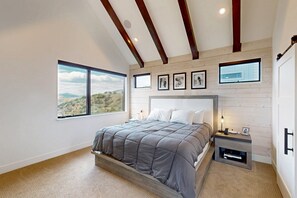 A bedroom with a large bed, a nightstand, a window with a view, and wooden beams on the ceiling. - Sunlight home with private hot tub, game room and EV charger (Steamboat Springs)