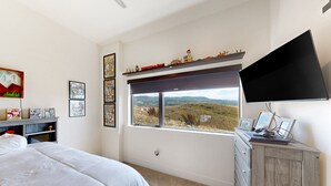 A bedroom with a bed, a dresser, a TV, and a window with a view of the countryside. - Spacious 4BR retreat with hot tub, game room, and great location (Steamboat Springs)