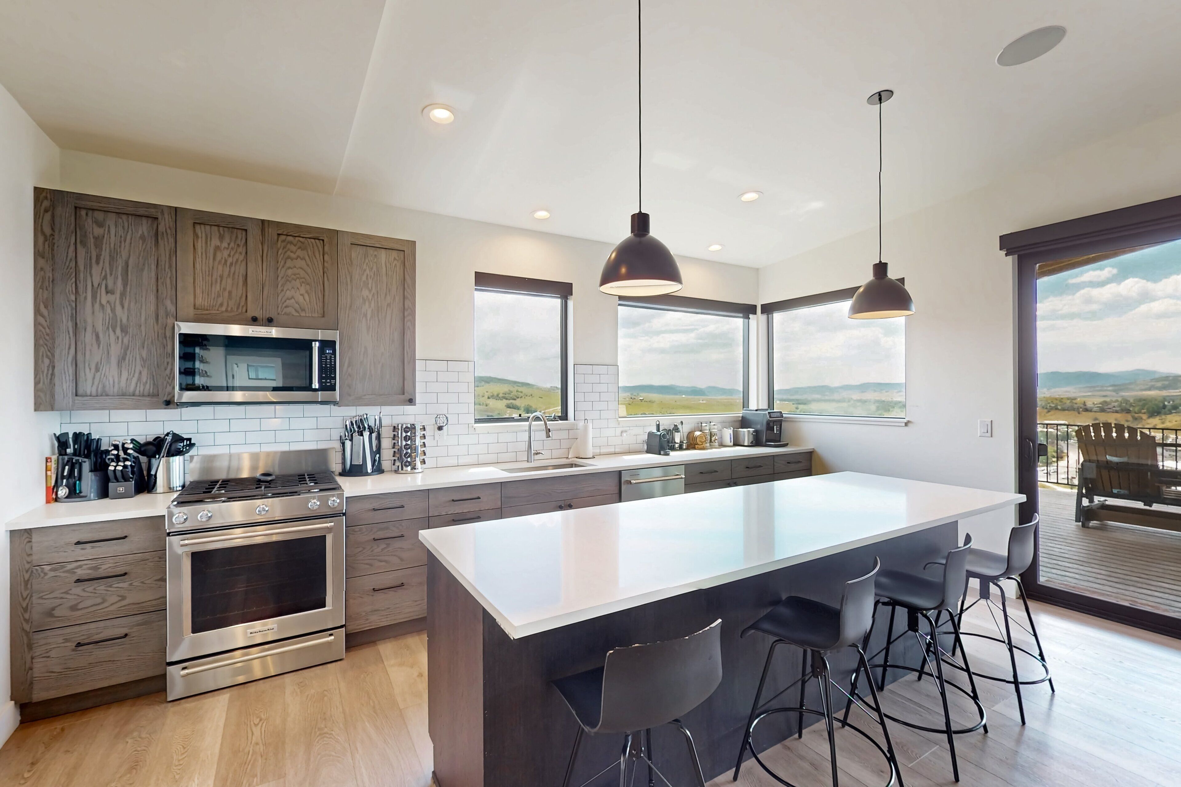 A modern kitchen with a central island, stainless steel appliances, and a large window offering a view.