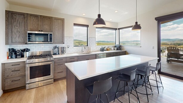 A modern kitchen with a central island, stainless steel appliances, and a large window offering a view. - Spacious 4BR retreat with hot tub, game room, and great location (Steamboat Springs)