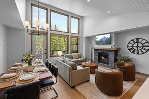 A modern living room with a fireplace, large windows, and a dining area set up for a meal. - Spring Creek Vacations 4 BR Villa TMV18 (Canmore)