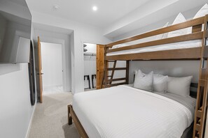 A bunk bed with white bedding, a wooden headboard, and a television mounted on the wall. - Spring Creek Vacations 4 BR Villa TMV24 (Canmore)
